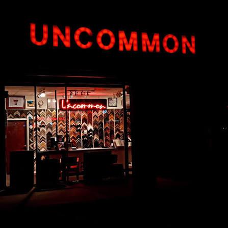 The illuminated Uncommon storefront on 34th Street at night, its neon sign glowing above the window and the moulding wall lit inside
